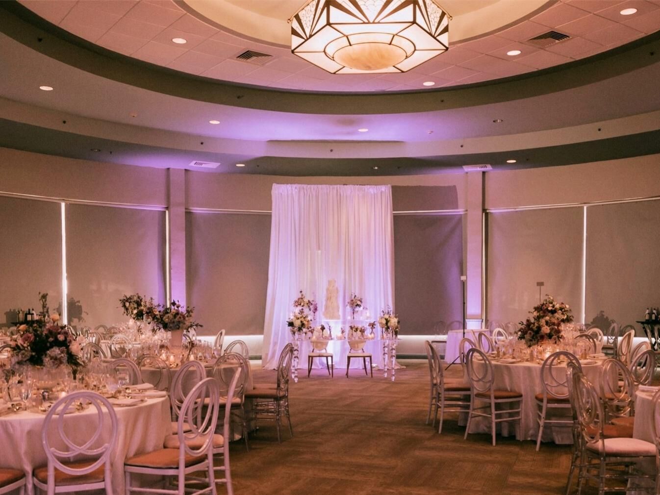 Une salle de banquet avec des tables rondes, des chaises et une scène décorée de draperies.