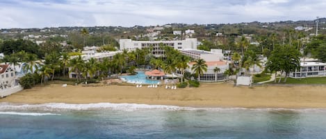 A beachfront hotel with a swimming pool, palm trees, and a view of the ocean.