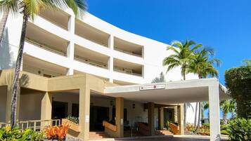 A multi-story hotel with a covered entrance, palm trees, and a clear blue sky.