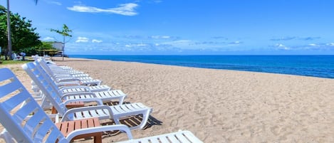 A beach with rows of white lounge chairs and a palm tree.