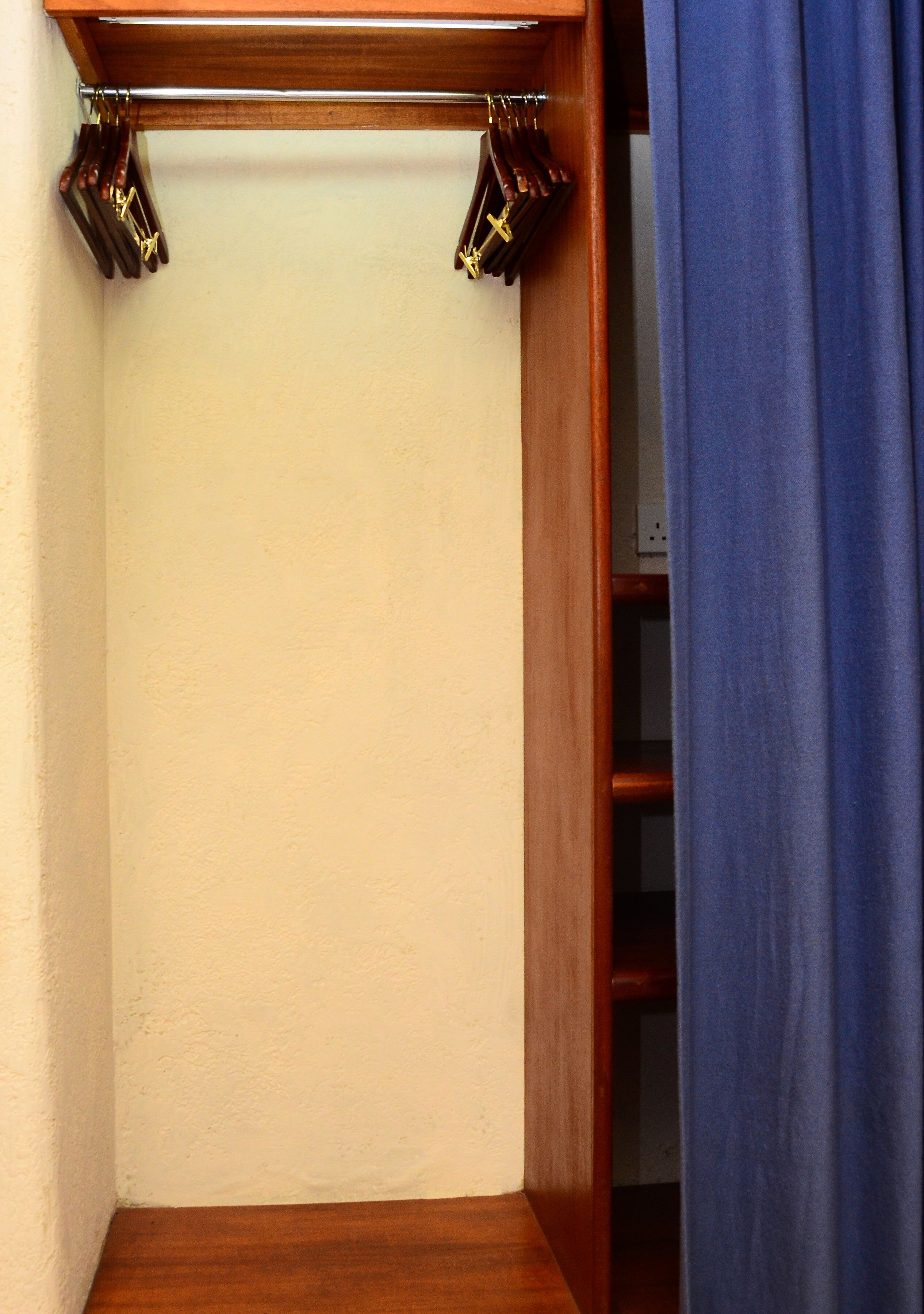 A corner of a room with a wooden shelf and a blue curtain.