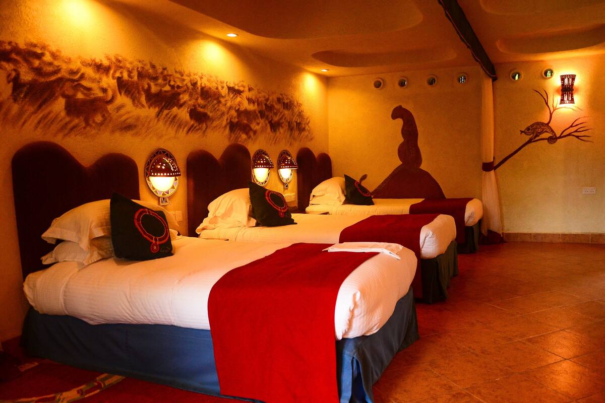 Une chambre d’hôtel avec trois lits, chacun recouvert d’une couverture rouge et de draps blancs.