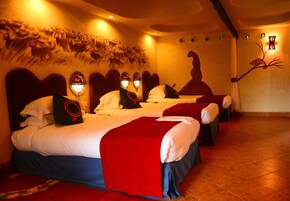 Habitación de hotel con tres camas, cada una con una manta roja y ropa de cama blanca.