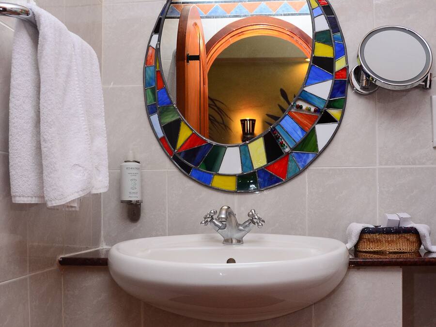 Un baño con un espejo redondo, dos lámparas de pared, un lavamanos y un perchero para toallas.