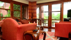 A spacious living area with large windows, a wooden coffee table, and red upholstered furniture. - Amboseli Serena Safari Lodge (Amboseli)