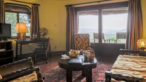A cozy living room with a television, a fan, a table with a basket of fruit, and a view of the outdoors.