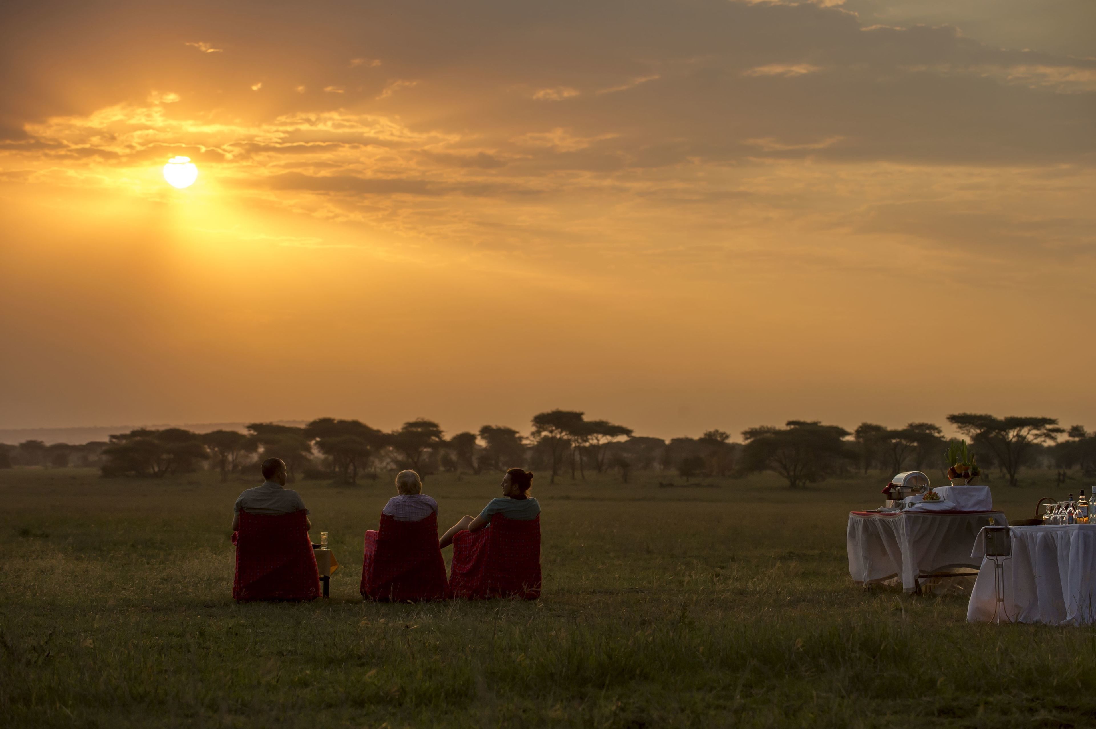 A sunset over a grassy field with a table set for a meal.