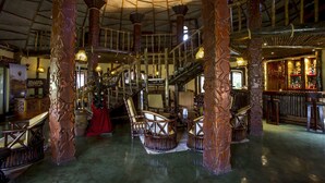 A spacious interior with high wooden pillars, a bar area, and seating arrangements.
