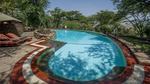 A swimming pool with a curved edge, surrounded by a stone wall and a wooden deck with lounge chairs.
