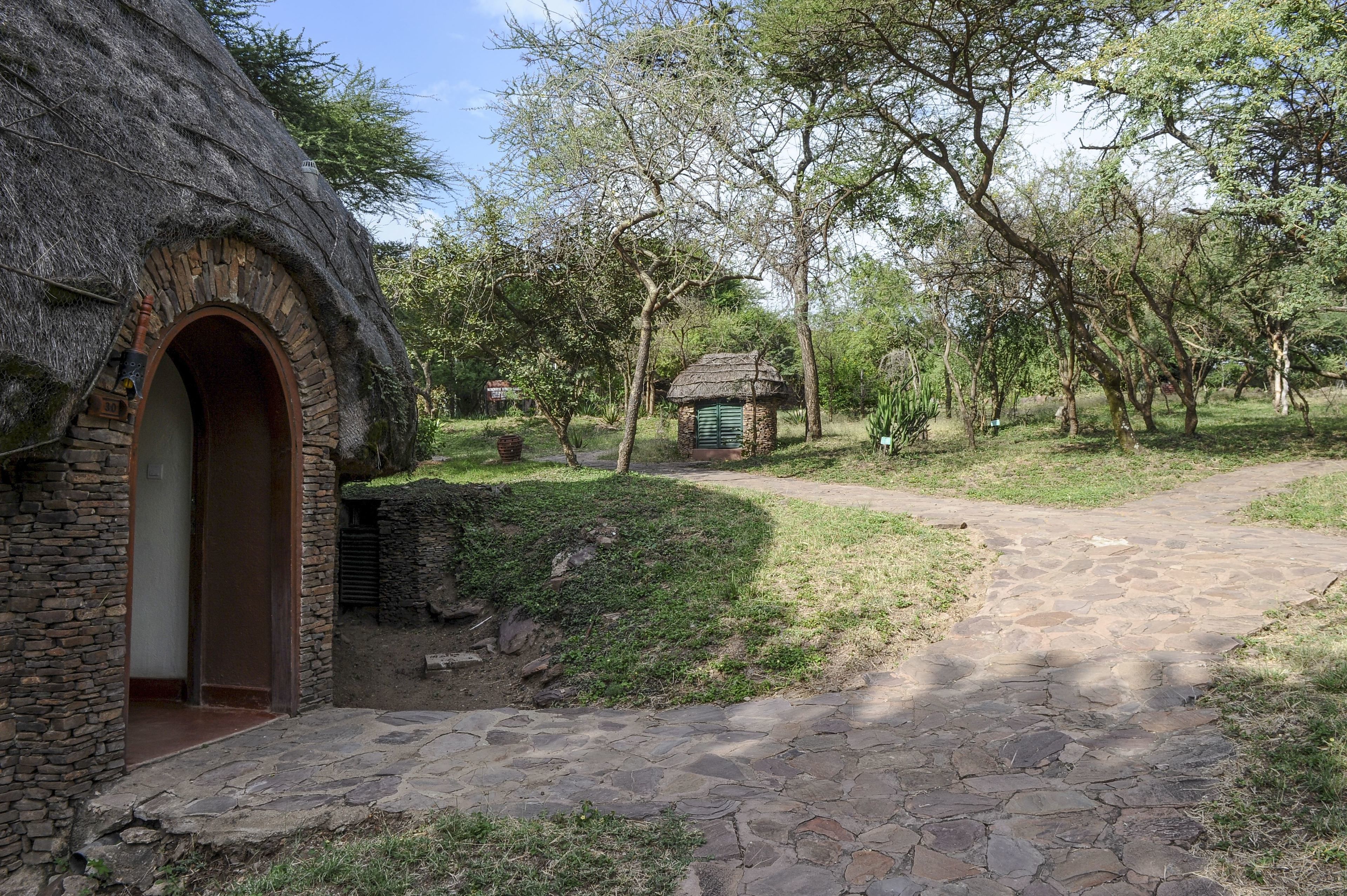 A rustic stone building with a thatched roof, a stone pathway, and a small structure in the distance.
