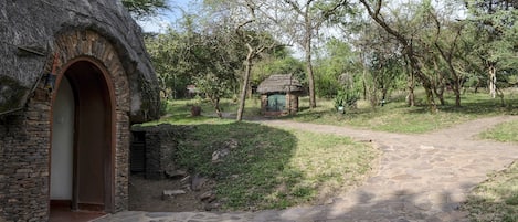 A rustic stone building with a thatched roof, a stone pathway, and a small structure in the distance.