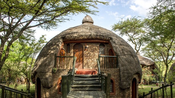 A traditional thatched-roof hut with a stone base, wooden steps leading up to a door, and a small porch area.