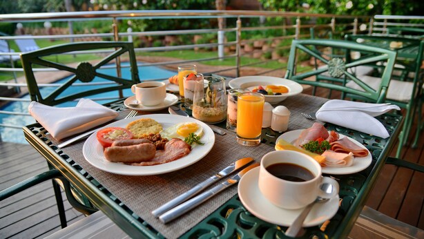 Una mesa de desayuno con platos de comida, tazas de café y un vaso de jugo de naranja.