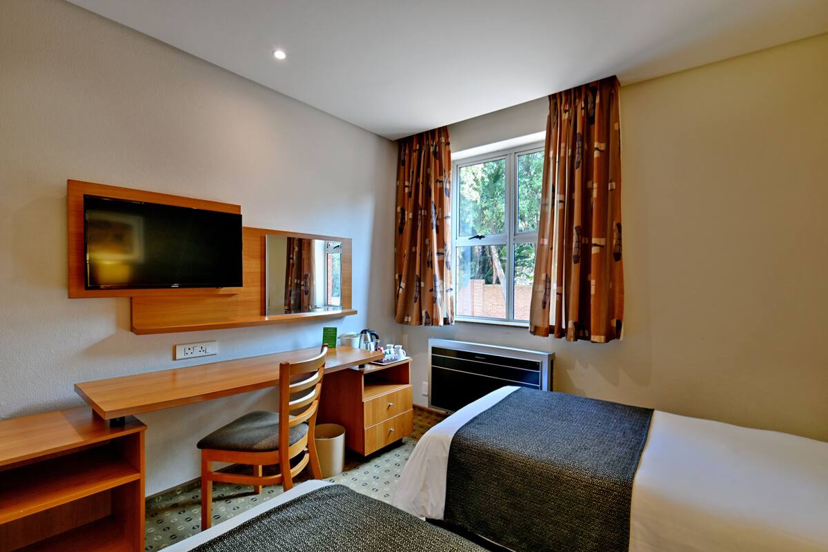 Habitación de hotel con cama, escritorio, silla, televisor y ventana con cortinas.
