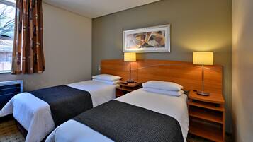 Habitación de hotel con dos camas, cabecera de madera, un cuadro y dos lámparas de noche.