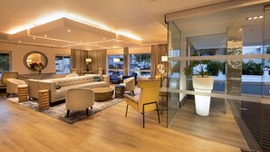 Un salon moderne avec un canapé, des fauteuils et une table basse. Une grande fenêtre offre une vue sur la ville.