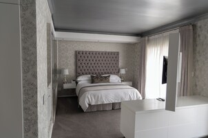 A modern hotel bedroom with a tufted headboard, a large bed, bedside tables with lamps, and a large mirror.
