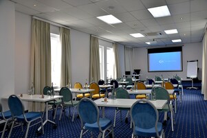 A conference room with multiple tables and chairs, a projector screen, and a presentation area.