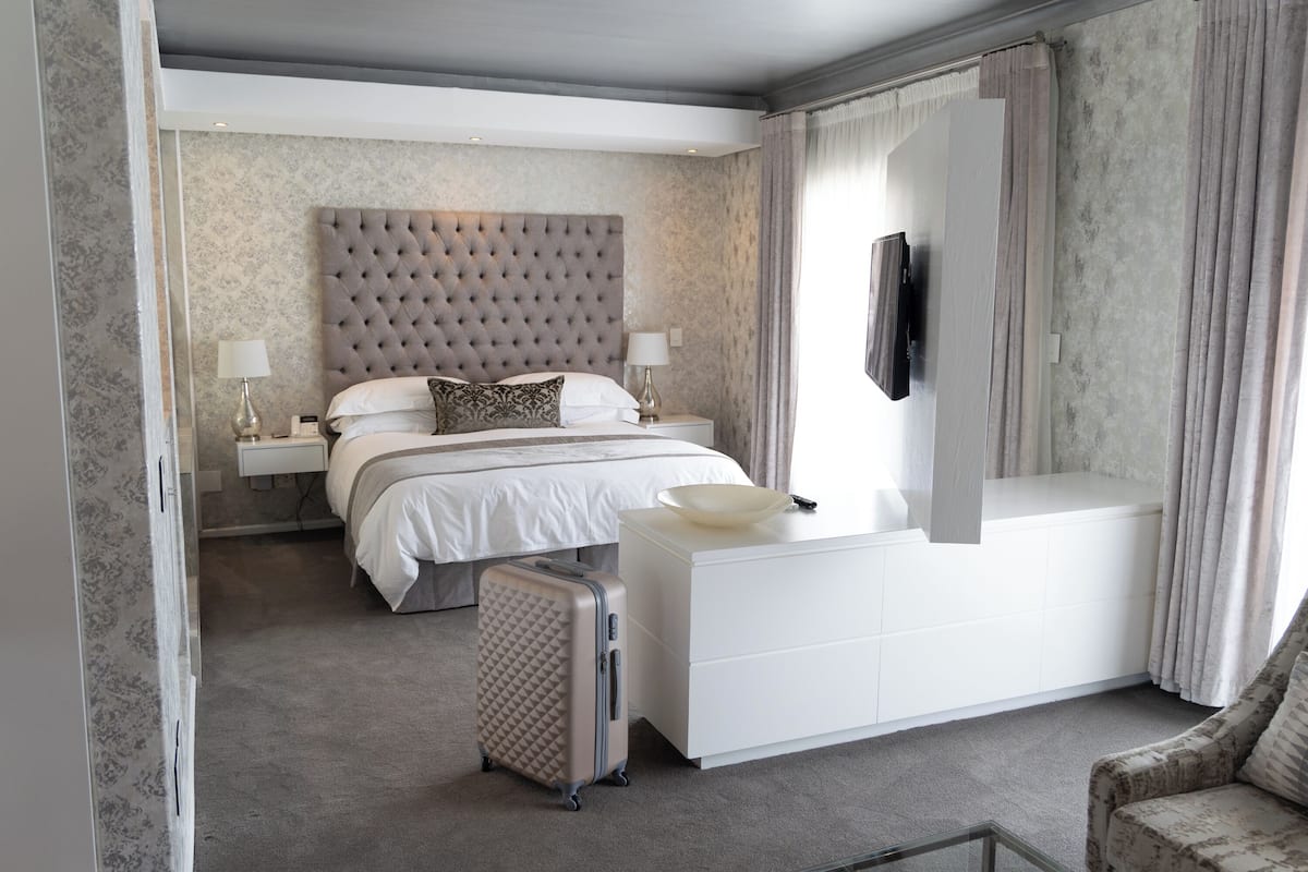 A modern hotel room with a large bed, a white dresser, a small table, and a chair.