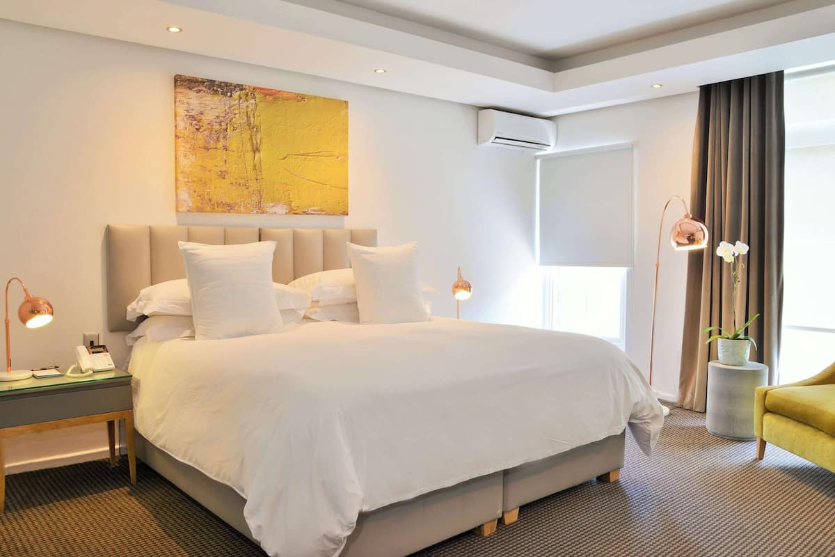 A modern hotel room with a large bed, bedside lamps, a small table with a phone, and a potted plant.