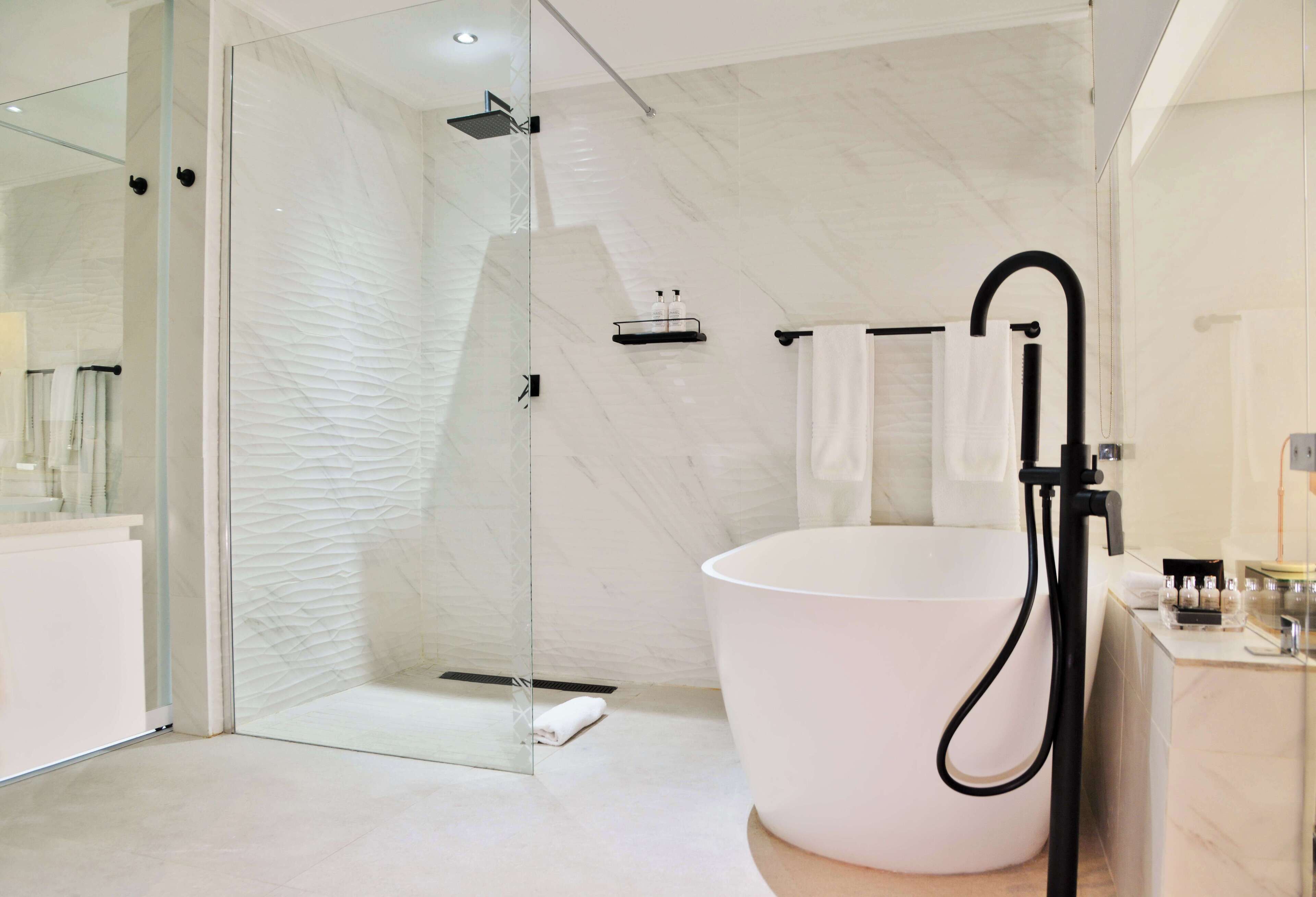 A modern bathroom with a glass-enclosed shower, a large white bathtub, and a marble-tiled wall.