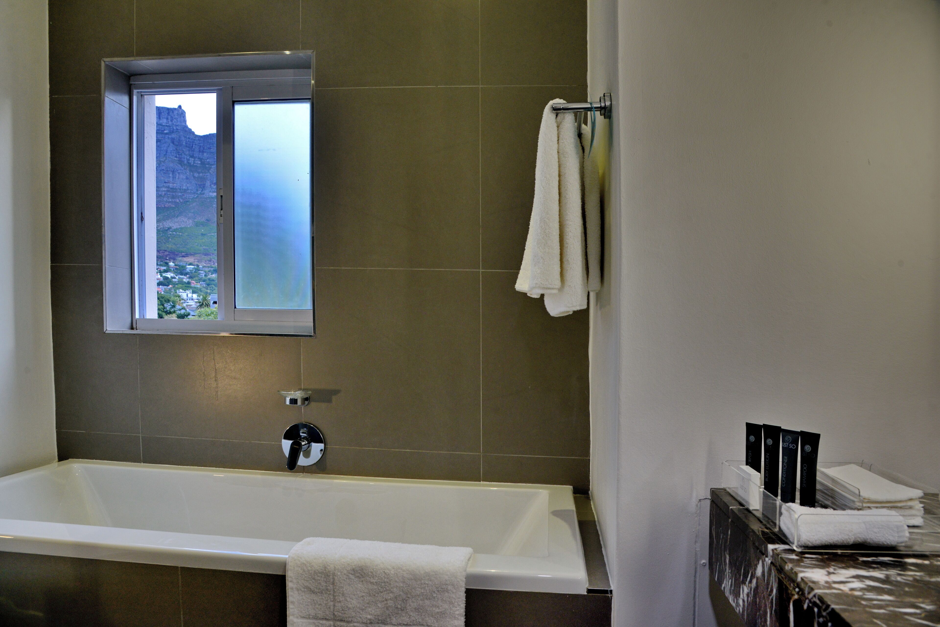 A modern bathroom with a bathtub, a window with a view of a mountain, and a towel rack with towels.