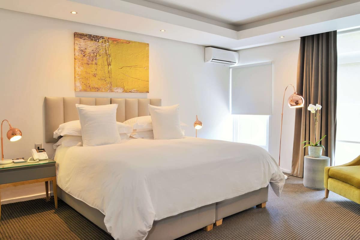 A modern hotel room with a large bed, bedside lamps, a small table with a phone, and a potted plant.