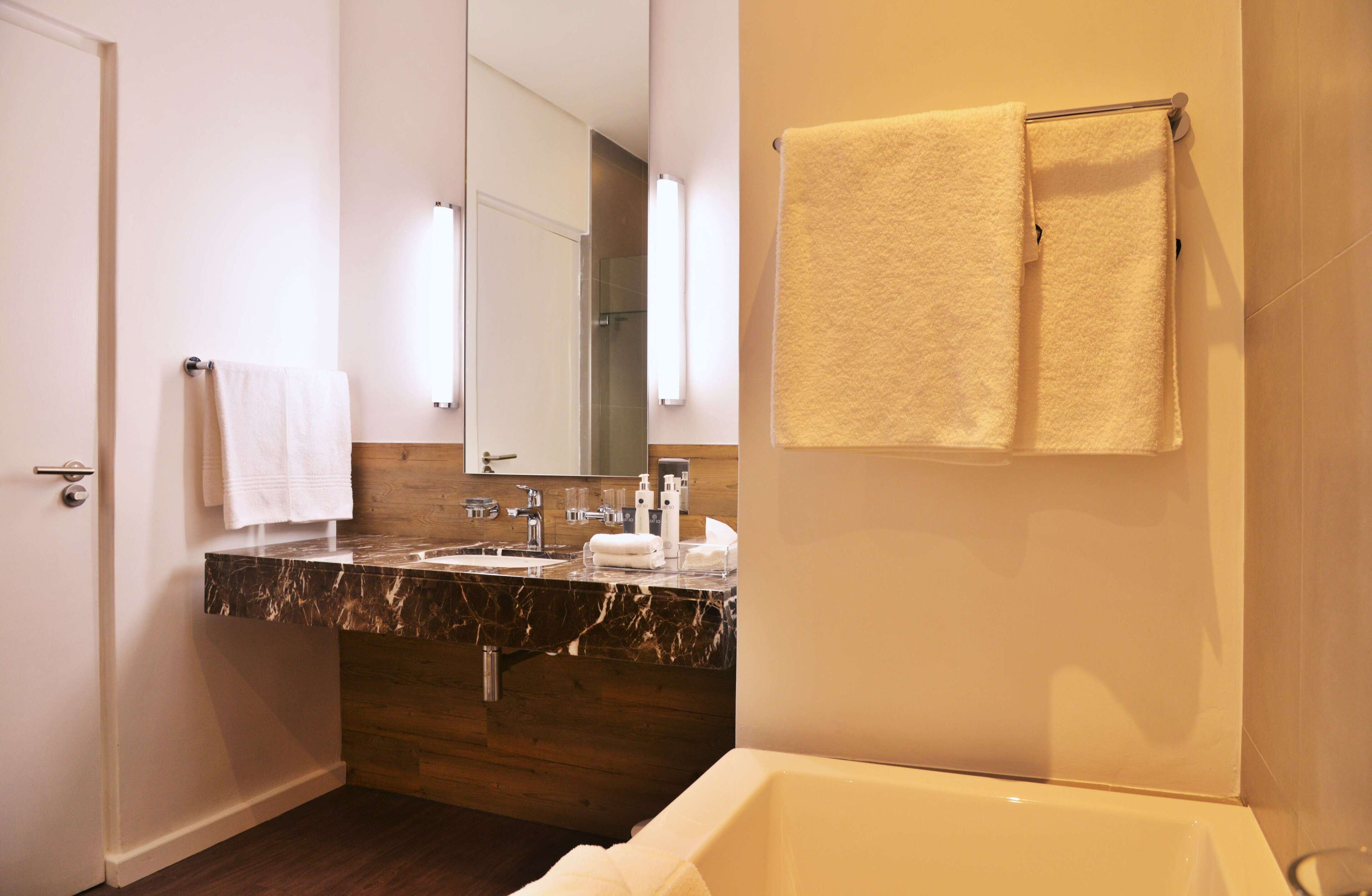 A modern bathroom with a marble countertop, wooden vanity, a large mirror, and a bathtub.