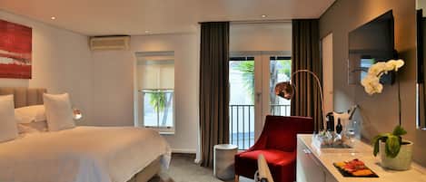 Ein Hotelzimmer mit Bett, Schreibtisch mit Pflanze, rotem Sessel und Blick ins Freie.