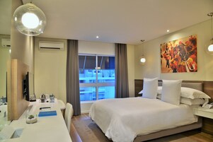 A hotel room with a large bed, a desk with a computer, a TV, and a window with curtains.
