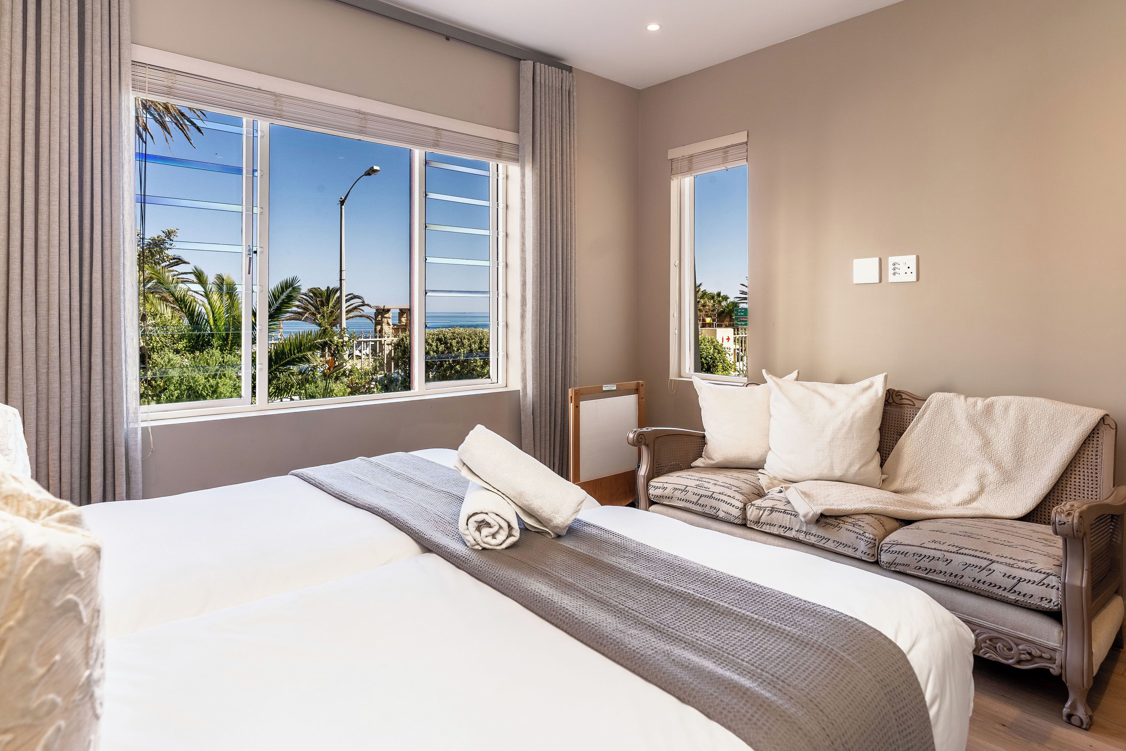 Une chambre d’hôtel avec un grand lit, un canapé et une fenêtre donnant sur des palmiers et la mer.