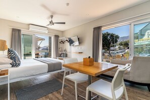 A modern hotel room with a bed, a desk, a chair, a table, a TV, and large windows offering a view of the city. - Camps Bay Village (Cape Town)