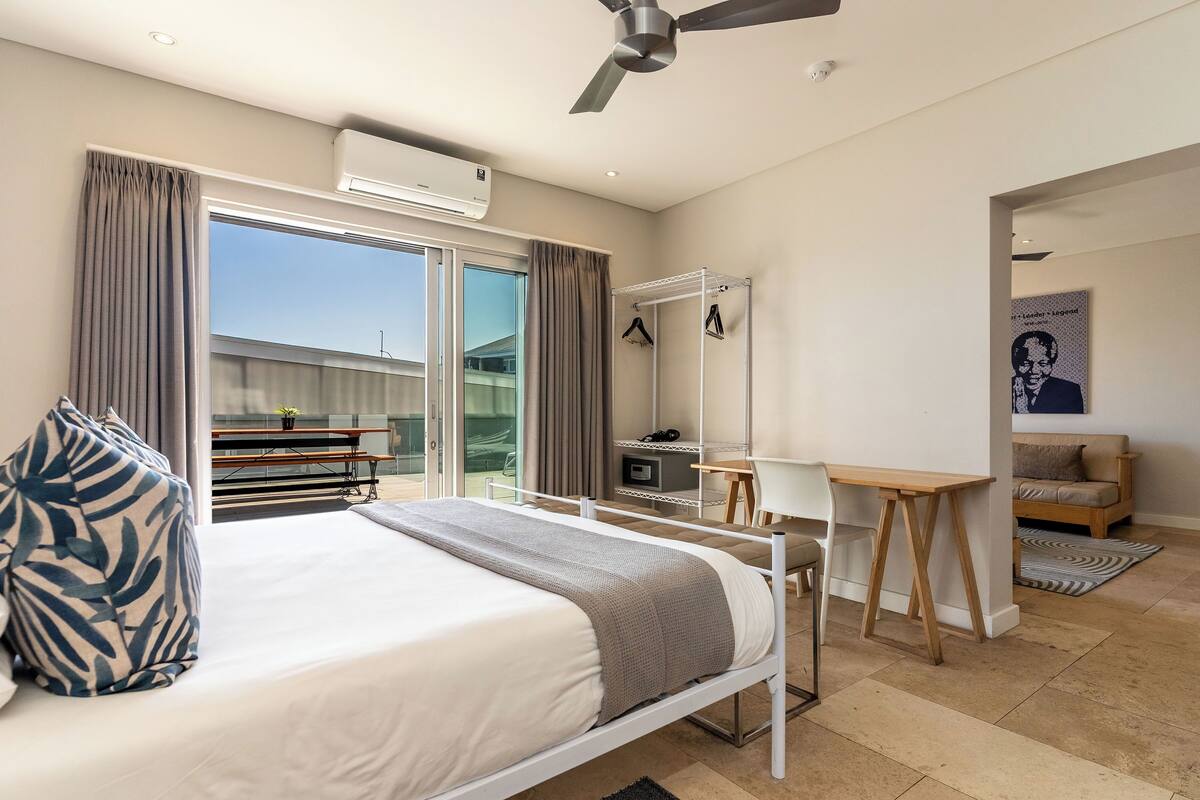 Una habitación de hotel moderna con cama, escritorio, silla, ventilador de techo y un gran ventanal.
