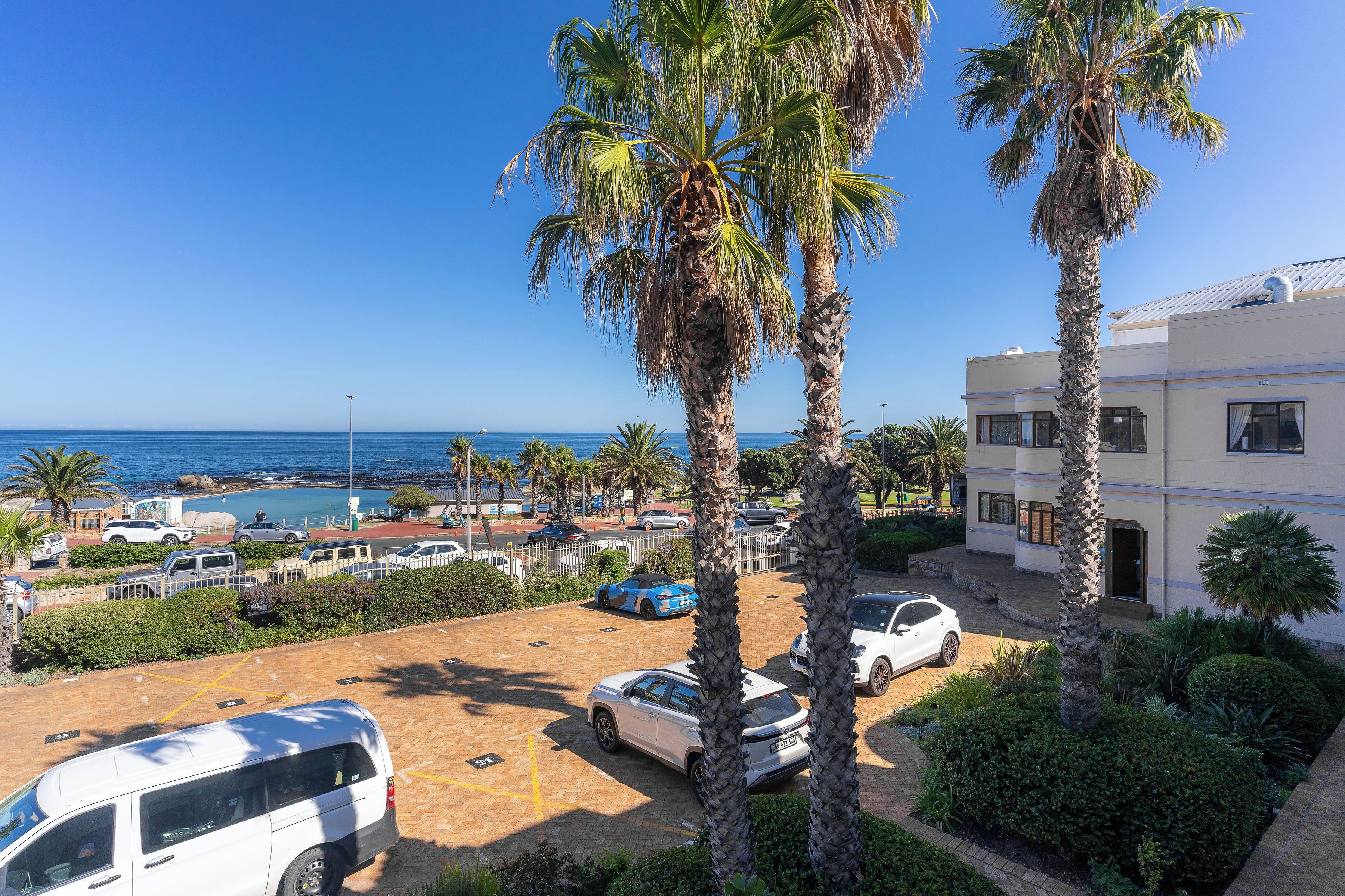 Een pand aan de kust met een parkeerplaats, palmbomen en uitzicht op zee.