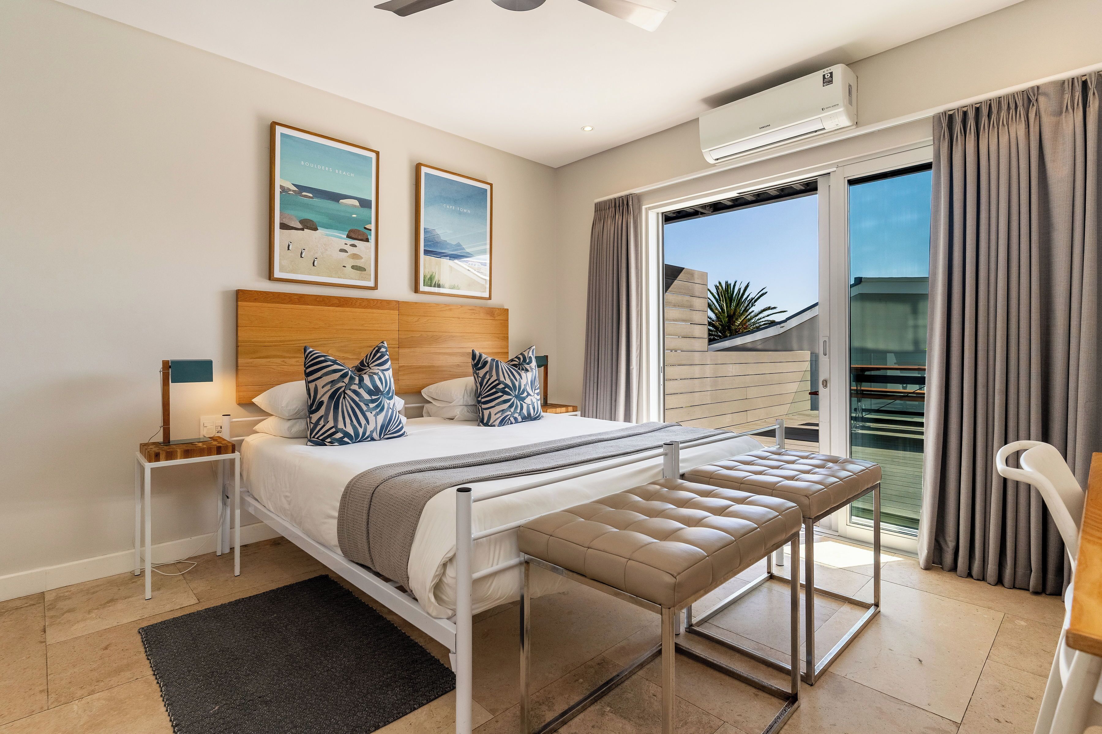 A bedroom with a bed, bedside tables, a bench, a window with curtains, and a view of the outdoors.