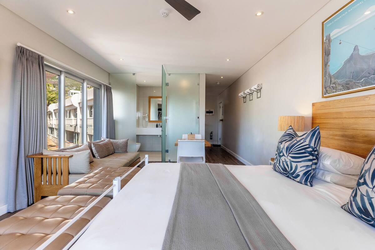 Habitación de hotel moderna con una cama grande, un área de descanso con vistas, una mesita y un cuadro en la pared.