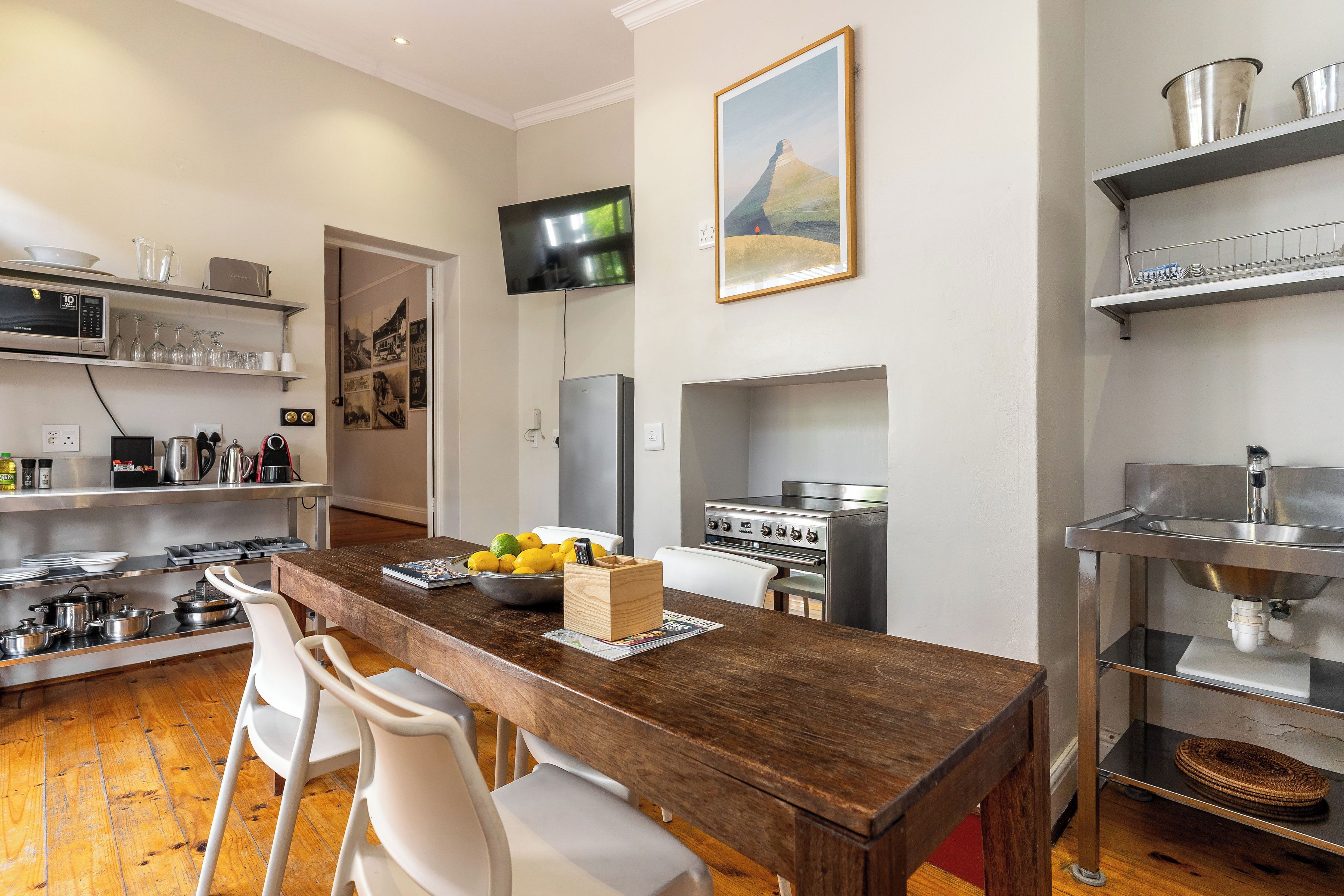 A modern kitchen with a wooden dining table, white chairs, stainless steel appliances, and a mounted TV.