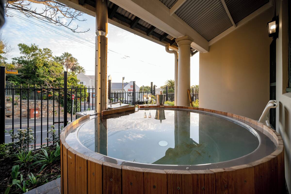Una bañera caliente con revestimiento de madera, un patio cubierto y vistas a la calle y edificios al fondo.