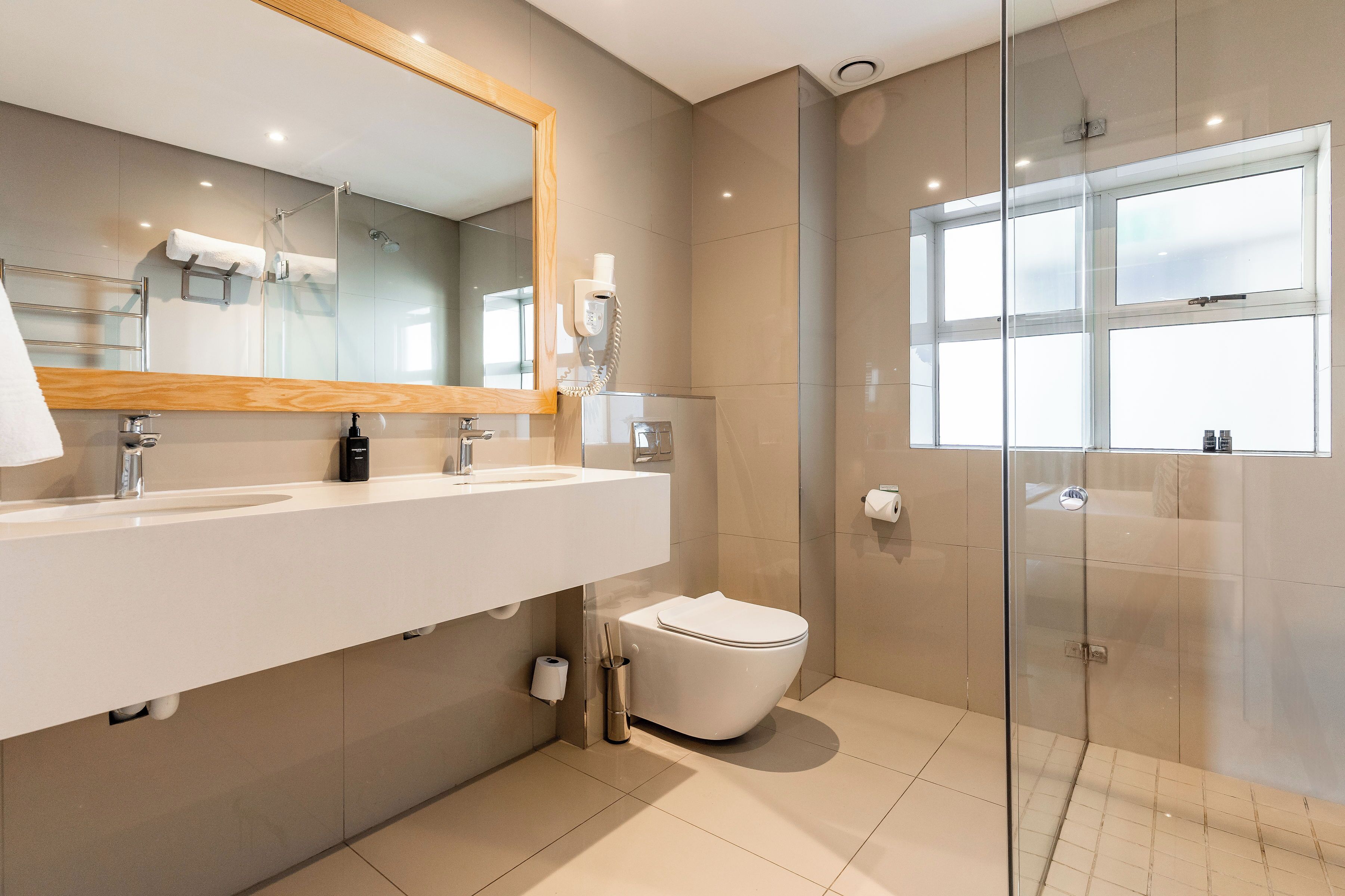 A modern bathroom with a large mirror, two sinks, a toilet, and a glass shower enclosure.