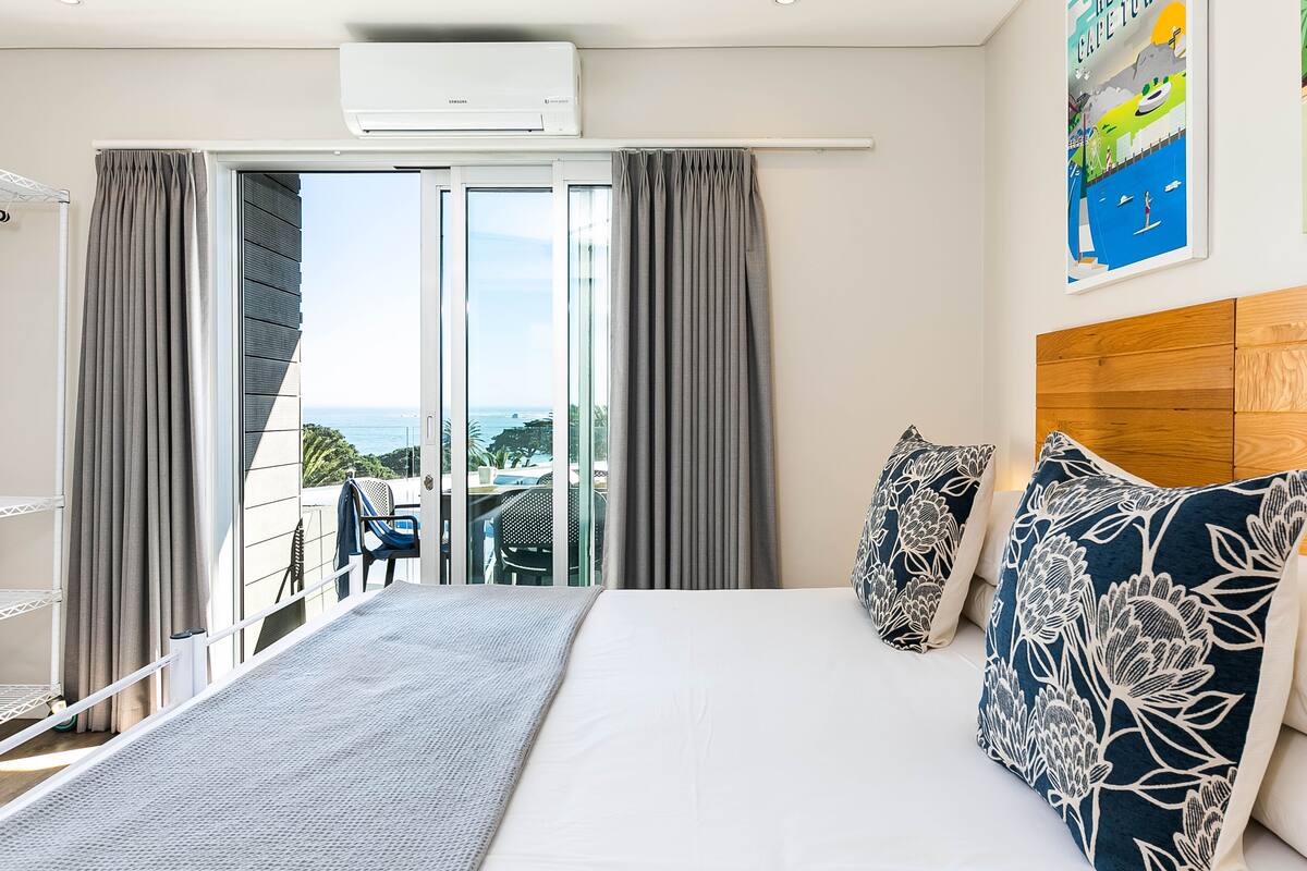 A hotel room with a bed, a view of the sea, and a balcony with a chair.