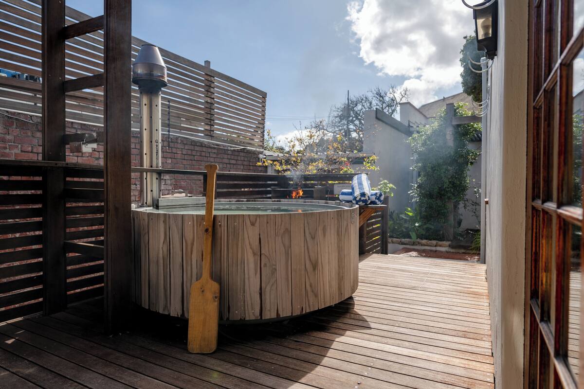 Un jacuzzi en una terraza de madera con una valla de madera y un muro de ladrillo al fondo.