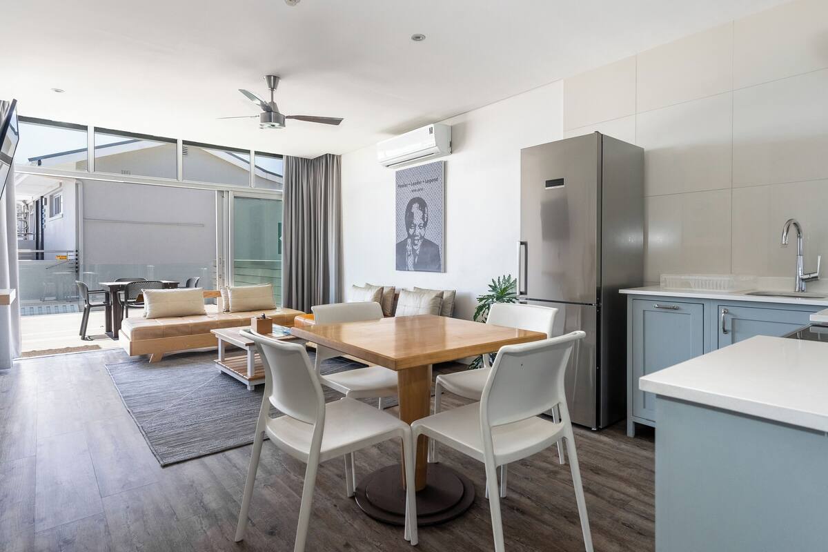 A modern kitchen with a dining area, a refrigerator, and a ceiling fan.