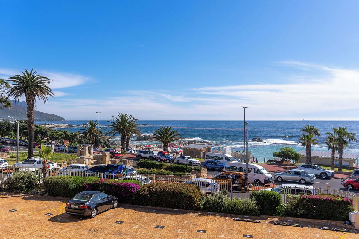 A coastal parking area with multiple cars, palm trees, and a view of the sea.