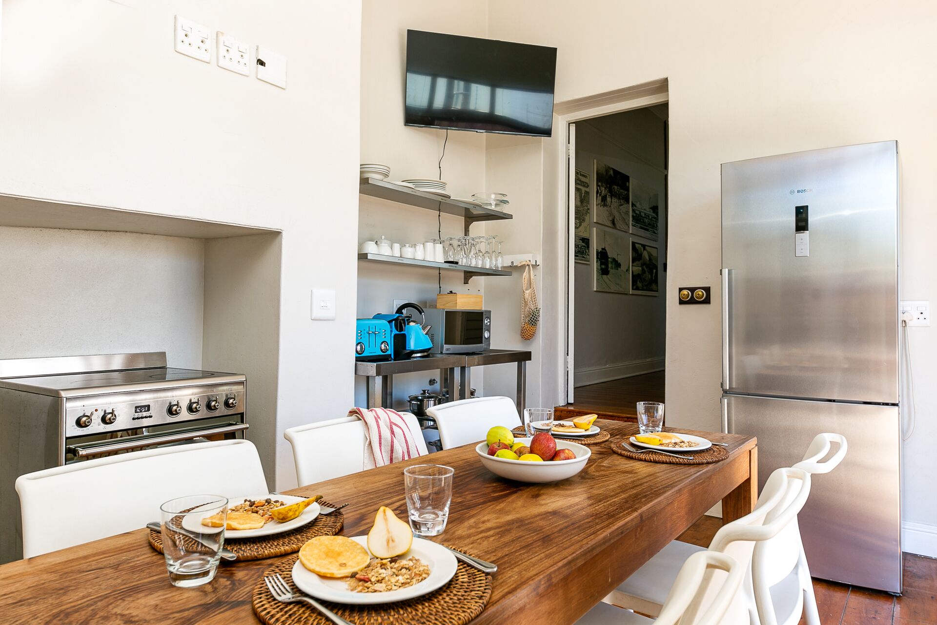 A modern kitchen with a stainless steel stove, a refrigerator, and a dining table set for breakfast.