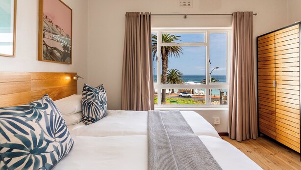A bedroom with a bed, a window with curtains, a view of the ocean, and a wooden headboard.
