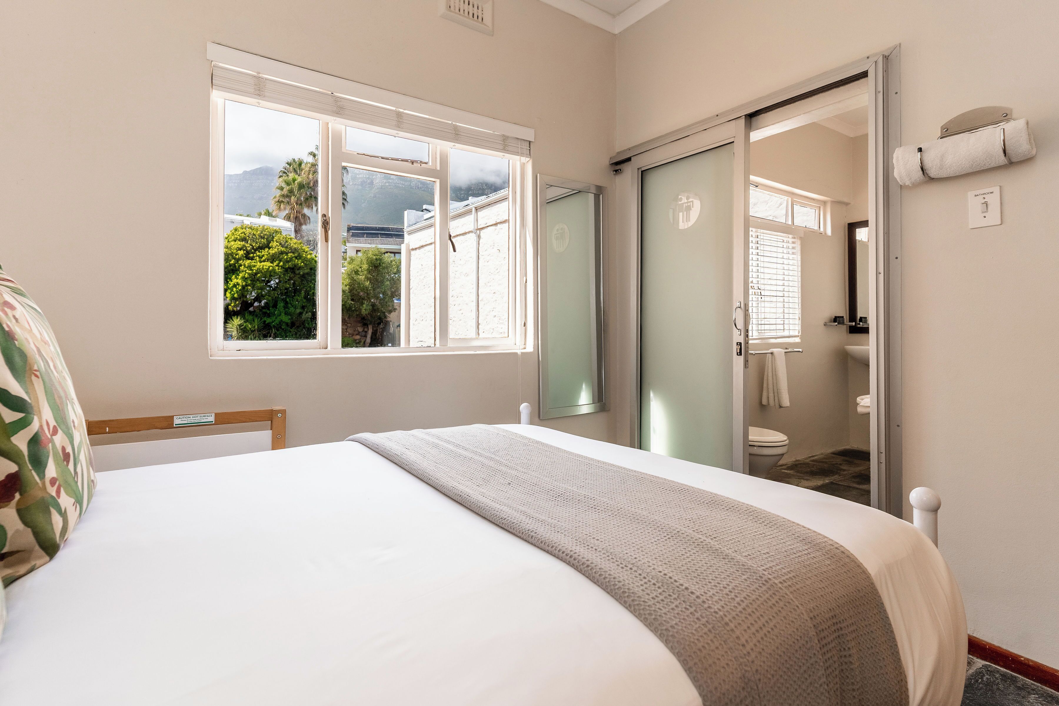 A bedroom with a bed, a window, a bathroom, and a view of greenery outside.