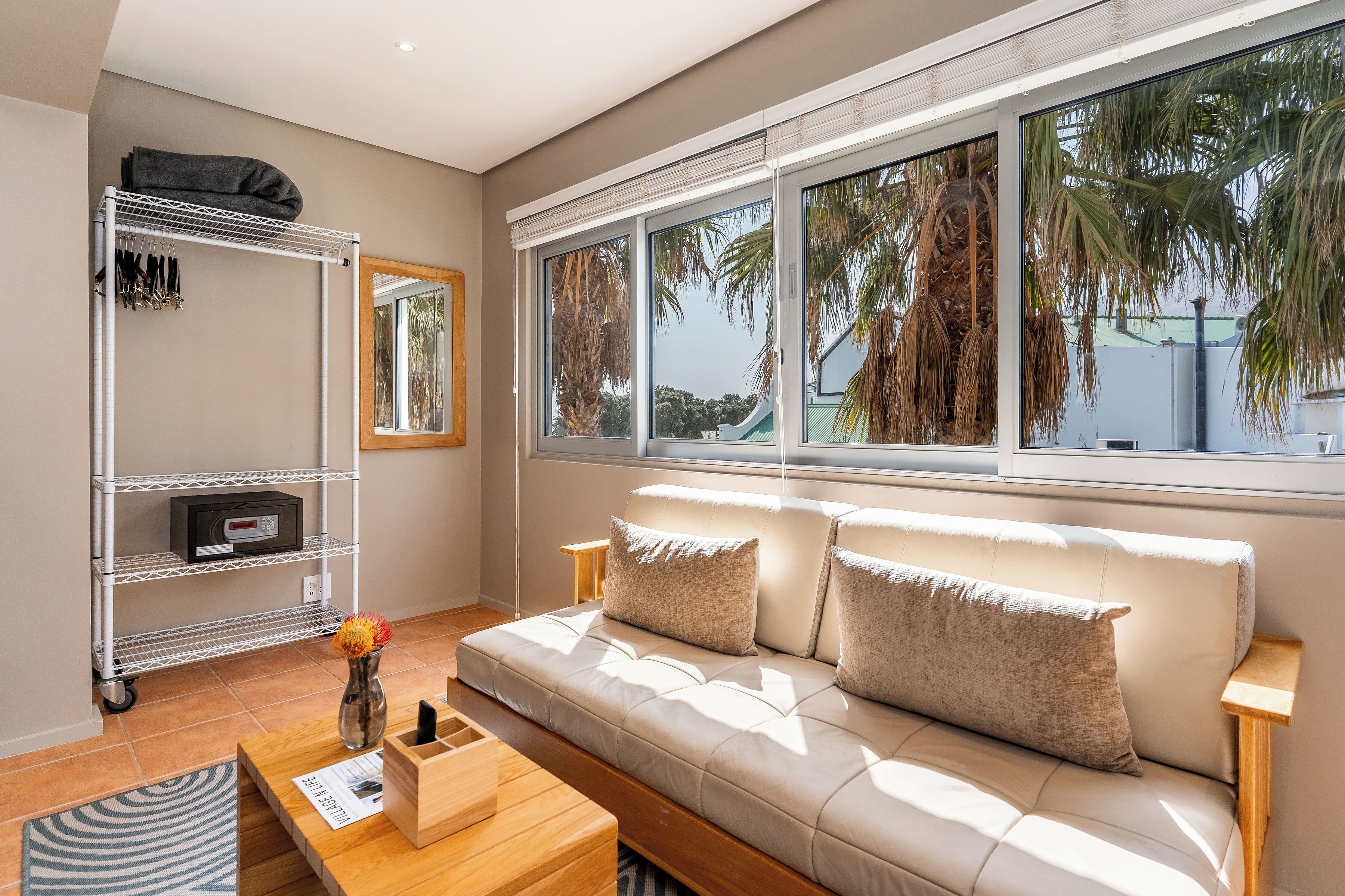 A modern living room with a sofa, a coffee table, a TV, and a window with a view of palm trees.