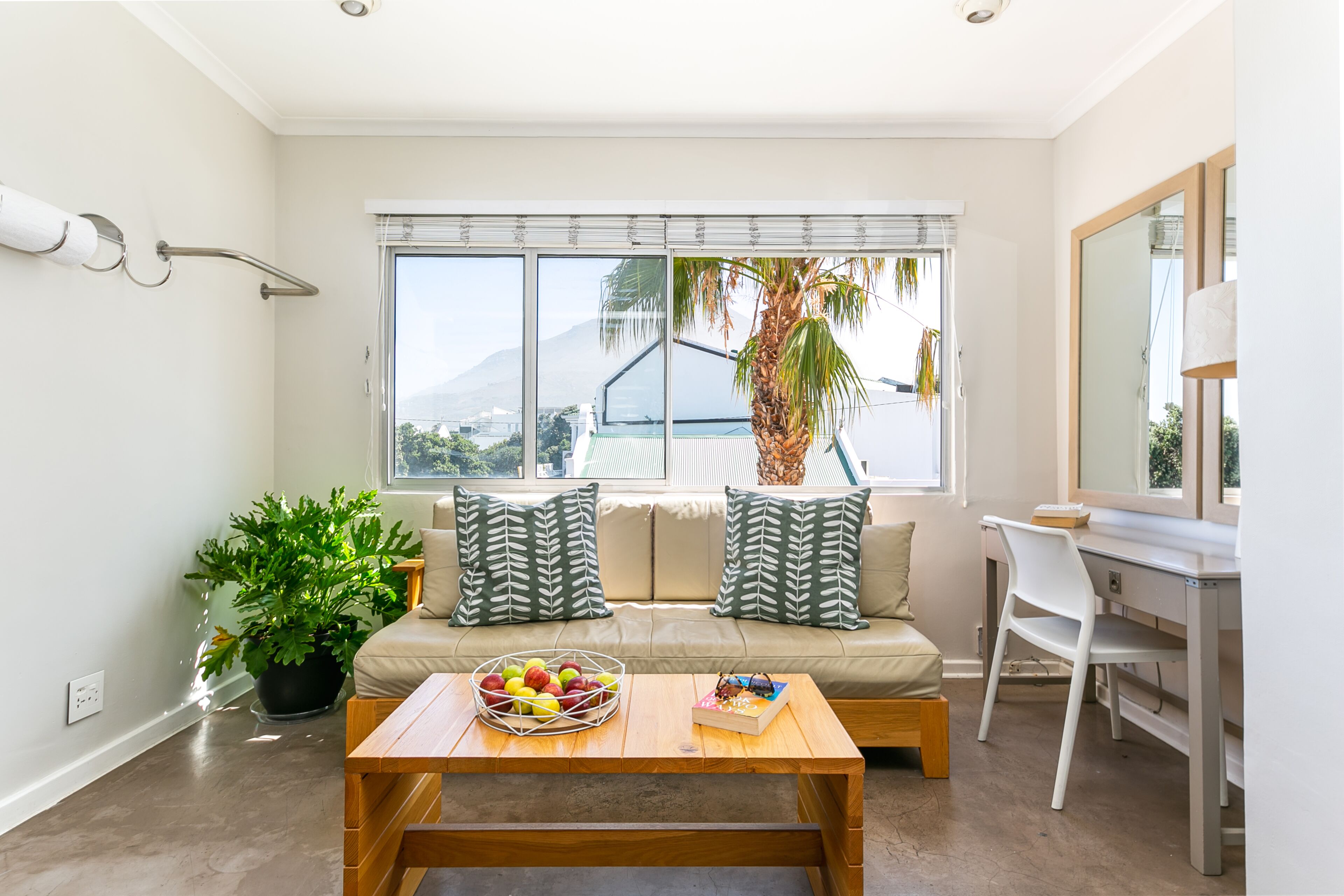 A modern living room with a sofa, a coffee table with fruit, a desk, and a large window with a view of mountains.