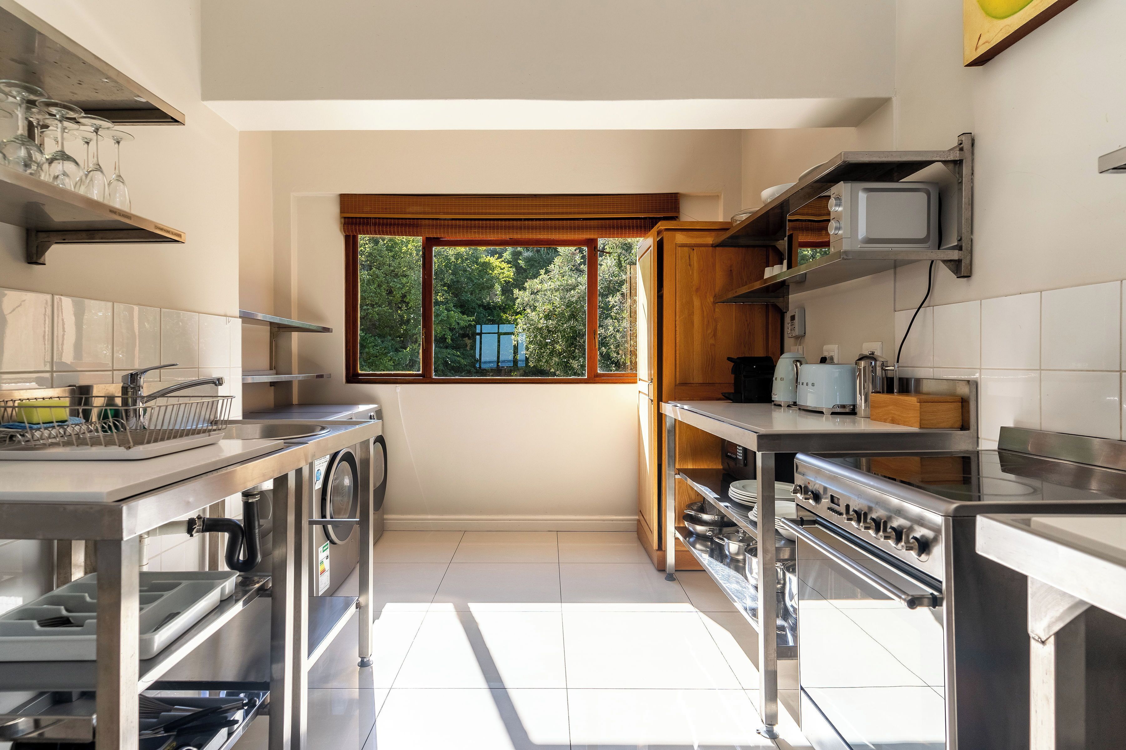 A modern kitchen with stainless steel appliances, wooden cabinets, and a window providing a view of greenery.