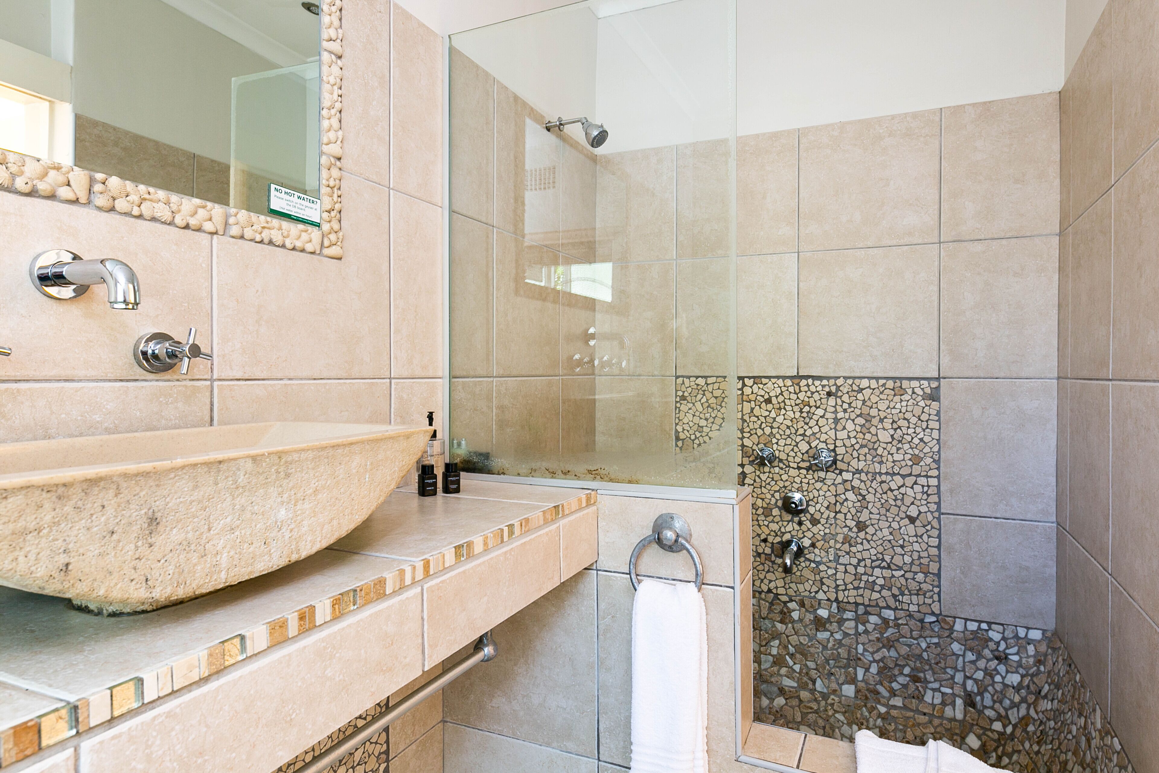 A bathroom with a large beige sink, a mirror, and a shower area with mosaic tiles.
